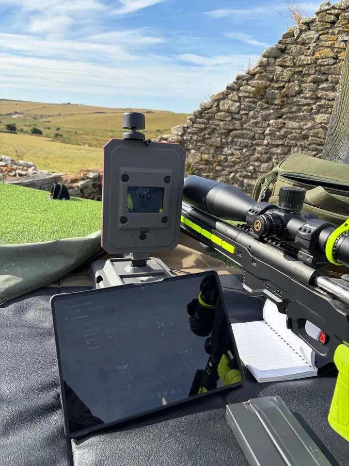 dopeology running on a tablet at the range, beside a chronograph and a scoped rifle on the bench